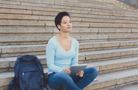 Young Woman Sits on Steps With Tablet in a City Setting During the Day