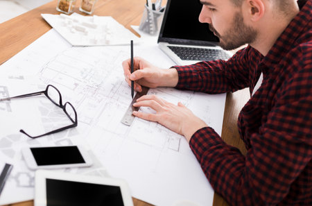Designer Creates Architectural Plans at Workspace With Devices and Tools Around Him