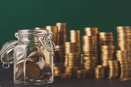 Collection of Gold Coins in Glass Jar With Stacks of Coins in Background at a Simple Settingの写真素材
