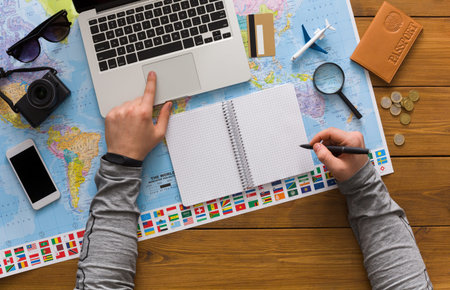 Planning a Travel Itinerary Using a Laptop and Map While Taking Notes in a Notebook