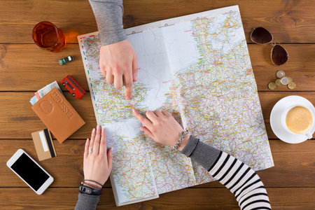 Friends Examining a Map and Planning a Trip at a Wooden Table With Drinks and Items Nearby