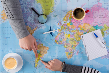Planning a Trip With a World Map on the Table, Coffee Cups, and a Notebook Present