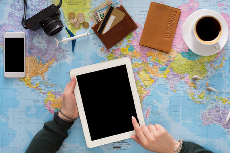 Planning a Trip Using a Tablet on a World Map With Travel Items and Coffee Nearby