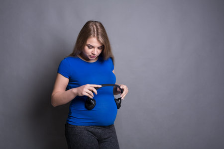 Pregnant Woman Holding Headphones While Standing in Front of a Gray Background