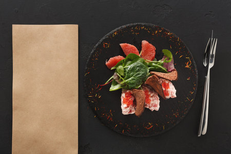 Delicate Dish of Meat and Greens Served on a Black Plate With Brown Paper Nearby