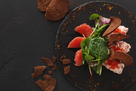 Salad With Bread and Citrus Fruits Served on a Dark Plateの写真素材