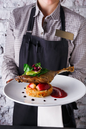 Waiter Serves Duck Dish With Vegetables and Sauce in a Restaurant on a Busy Evening in the Cityの写真素材