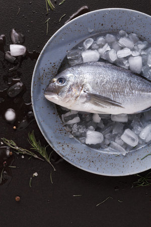 Fresh Fish Served on Ice With Herbs and Seasoning in a Bowl on a Dark Surface