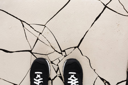 Unique View of Cracked Ground With Black Shoe Standing on a Light Surface During Daylight