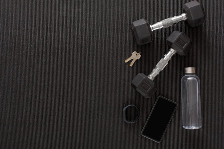 Two Dumbbells, a Water Bottle, Keys, and a Phone on a Workout Mat in a Gym Setting