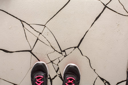Steps on Cracked Surface While Wearing Black Athletic Shoes With Pink Laces