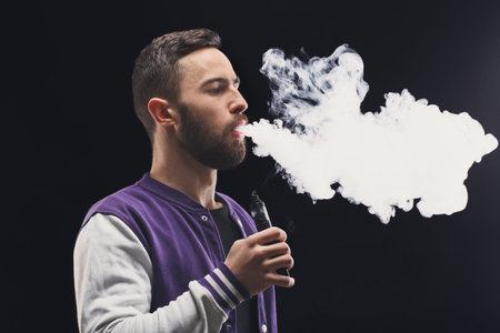 Young Man Vaping Indoors and Producing Large Clouds of Vapor During an Evening Session