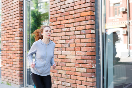Woman is Running Near a Brick Wall in an Urban Area During Daylight Hoursの写真素材