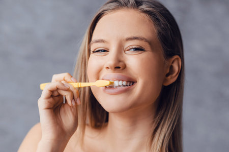 Smiling Woman Brushes Her Teeth With a Yellow Toothbrush in a Bright Setting
