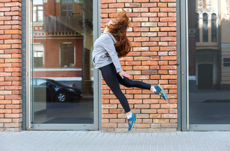 Person Jumps Outside a Brick Building Beside a Car in the Daytime