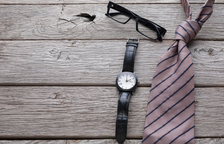 Timeless Items on a Wooden Table Showcasing a Watch, Glasses, and a Tie in Natural Lightの写真素材