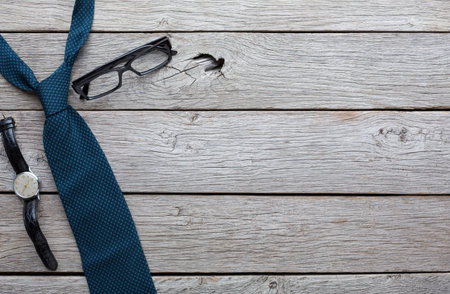Items on Wooden Table Show a Tie, Glasses, and Watch Arranged for a Work Settingの写真素材
