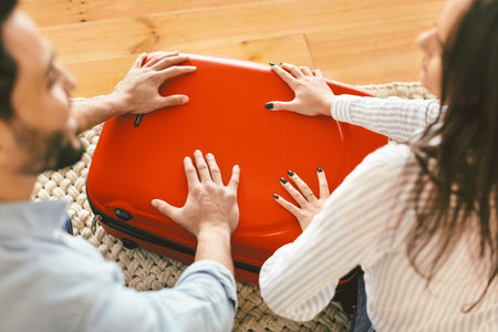 Getting ready for holidays. Hands of man and woman pushing on suitcase, trying to close it, packing clothes for tripの写真素材