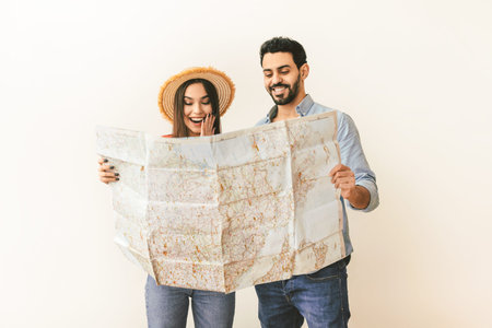 Young spouses choosing travel destination for vacation, standing with touristic map over light wall,...