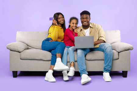 Family Enjoys Time Together While Using a Laptop and Holding a Credit Card at Homeの写真素材