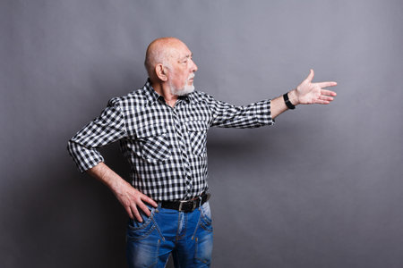 Elderly Man Gestures With Hand While Standing Against a Gray Background in Casual Attire