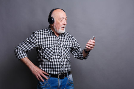 Elderly Man Listens to Music While Looking at His Smartphone in a Studio Setting