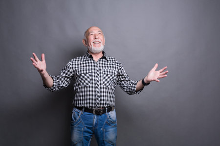 Older Man Smiles With Arms Raised Against Gray Background During Creative Session at Studio