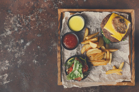 Tasty Burger With Cheese, Fries, and Sauces Served on a Wooden Trayの写真素材