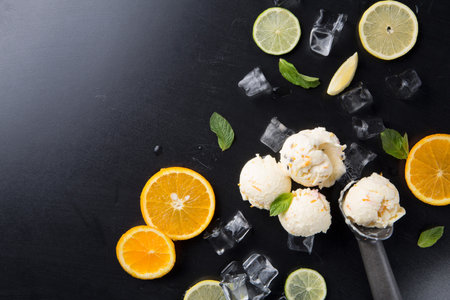 Creamy Ice Cream With Slices of Orange, Lime, Mint Leaves, and Ice Cubes on Black Surfaceの写真素材
