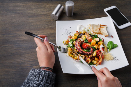 Enjoying a Meal of Grilled Octopus With Vegetables on a White Plate at a Dining Table
