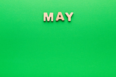 May Displayed in Wooden Letters on a Green Background With No Other Elements Present