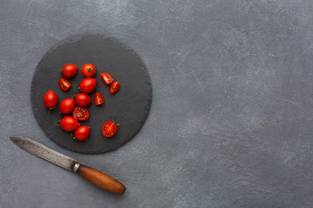 Slicing Small Red Tomatoes on a Round Slate Board With a Knife in a Kitchen Setting During the Dayの写真素材