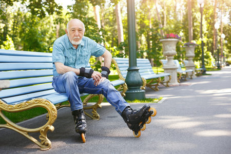 Man Sitting on Bench in Park Wearing Roller Skates and Protective Gear on a Sunny Day