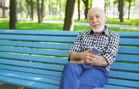Elderly Man Listening to Music While Sitting on a Park Bench During the Afternoon