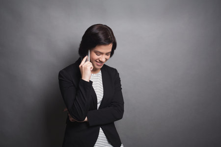 Woman Talks on Phone and Smiles While Standing in Front of Gray Background