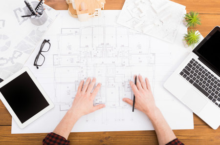 Hands of a Person Working on Architectural Plans in an Office Setting With a Laptop and Tablet
