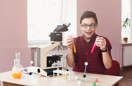 Boy Conducts an Experiment With a Microscope and Colorful Test Tubes in a Classroom Setting