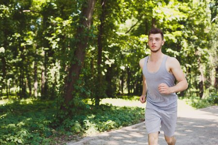 Runner Jogs Along Path in Green Forest During Sunny Day in Early Morning Hours