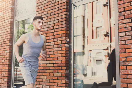 Man Runs by Brick Wall and Glass Windows in Urban Area During Sunny Afternoon