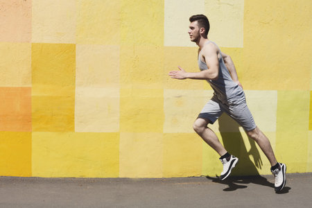 Young Man Runs Beside a Colorful Wall in Summer During the Day