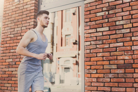 Young Man Jogs Near Brick Wall on Urban Street During Bright Daylight Hours