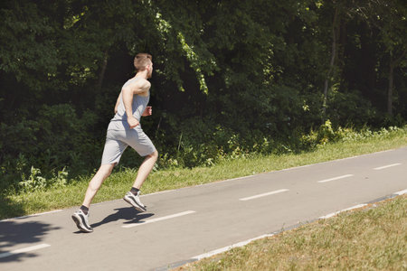 Man Running on a Path Through Green Trees on a Sunny Day in the Park