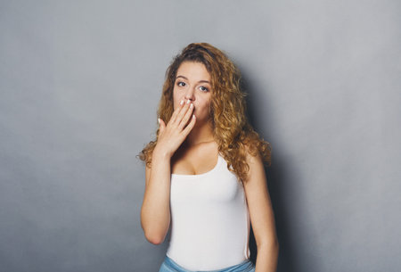 Young Woman Blowing a Kiss While Standing Against a Gray Background in a Casual Pose