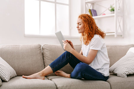 Woman Sitting on Couch Reading a Tablet in a Bright Living Room During the Day