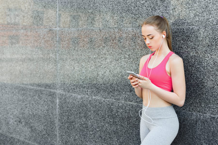 Young Woman Listens to Music While Standing Against a Wall in Outdoor Location During the Day