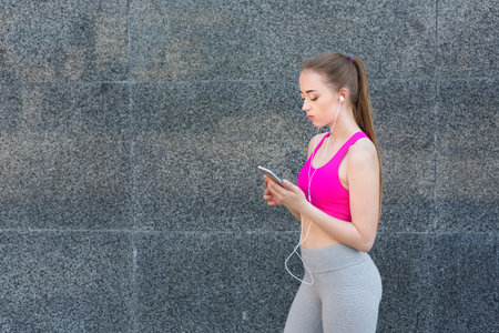 Young Woman Listens to Music While Walking in Front of a Stone Wall During Daytime