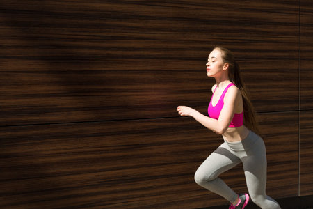 Female Runner in Workout Gear Moves Along a Brown Wooden Wall in the Daytime