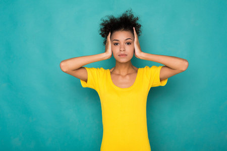 Young Woman Holds Her Head With Both Hands Against a Blue Background During an Indoor Session