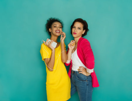 Two Friends Enjoying Music Together on a Bright Turquoise Background in a Playful Moment