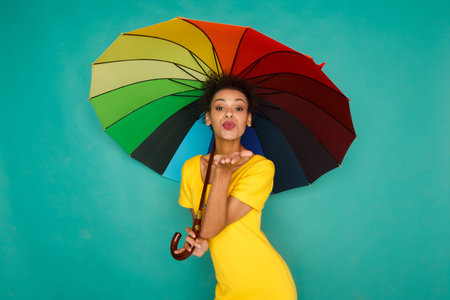 Woman Holds Colorful Umbrella and Blows Kiss in Bright Location